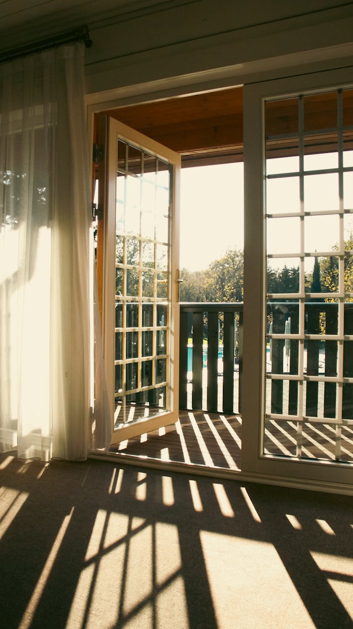 Warm sunlight streaming through open French doors onto a cozy balcony, casting playful shadows.