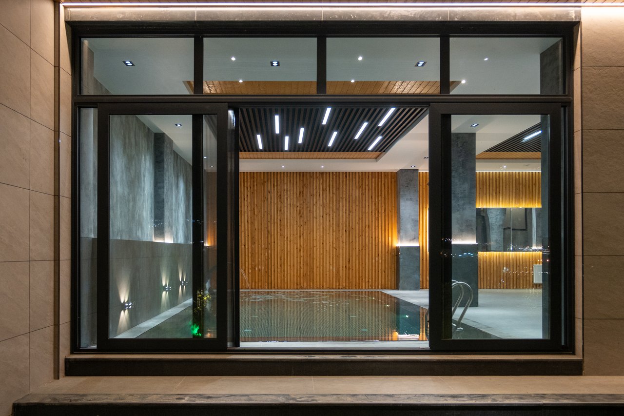 Elegant indoor pool area featuring modern lighting, wood paneling, and large glass windows for relaxation.