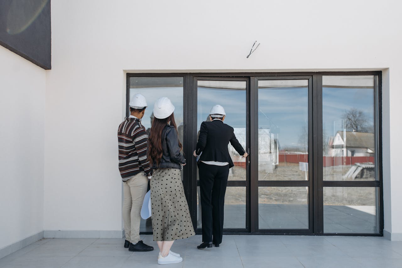 Real estate agents in helmets showing a new house to clients through glass doors.